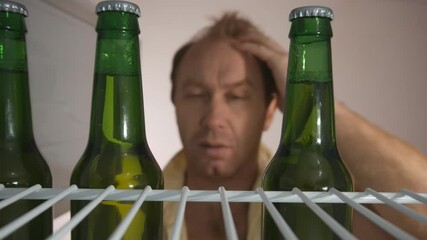 a young Caucasian man in the morning with a headache after drinking alcohol found three bottles of beer in the refrigerator, very happy and joyful took and left to continue the holiday
