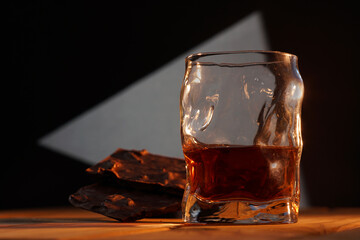 A glass of cognac and a bar of chocolate on a wooden table on a dark background