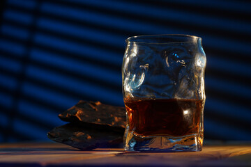 A glass of cognac and a bar of chocolate on a wooden table on a dark background