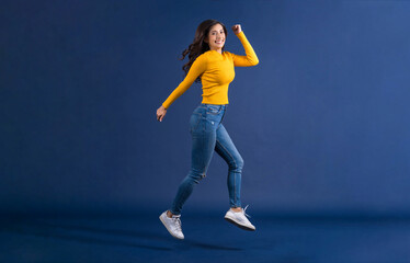 Fototapeta na wymiar Happy young Asian woman in colorful yellow color casual clothes jumping and running on blue color background, lifestyle and leisure, travel and tourist, travel and vacation,happiness and funny concept
