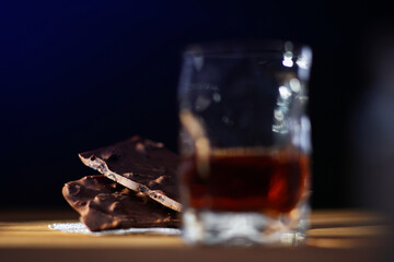 A glass of cognac and a bar of chocolate on a wooden table on a dark background