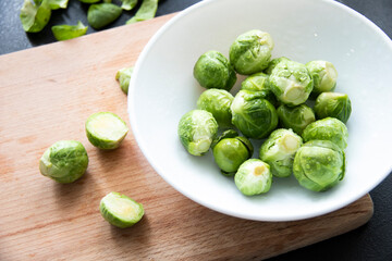 Brussels sprouts in a white bowl on a wood background. Top view, small cabbage, organic food, healthy food. Vegan food.