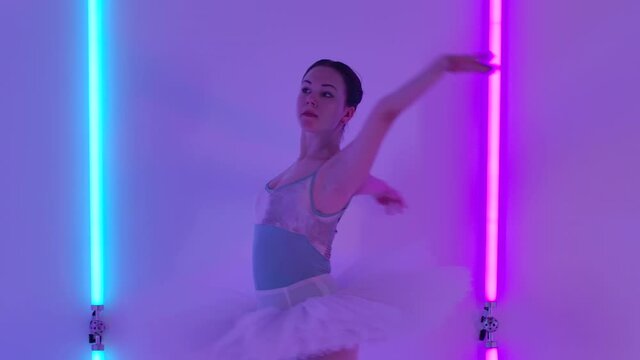 The ballerina rehearsing, performing tournant exersice. A ballet dancer practices various choreographic exercises in the studio against the backdrop of bright neon tubes. Slow motion. Close up.