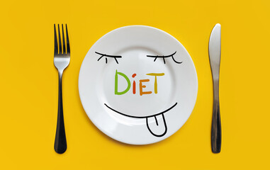 A white plate on which the word Diet is written standing on a yellow tablecloth and funny face is licked with hunger.The concept of a balanced diet, ration and medical fasting. Background, copy space.