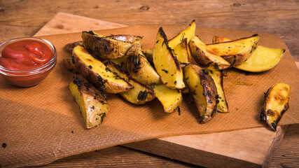 Rustic baked potato wedges and sauce on a wooden board on a wooden shabby table, close-up