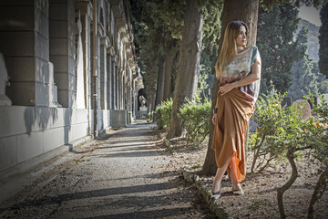 Beautiful Hispanic lady with ombre hair wearing a long summer dress and sandals in a cemetery © Ricardo Giancola/Wirestock