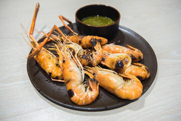 Grilled river shrimps with chili seafood sauce on black plate on wooden table.