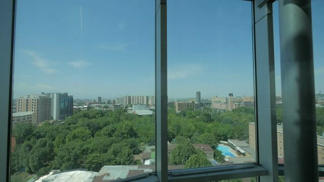 View of the city from a skyscraper glass elevator descending inside a business center with a glass roof. Elevator inside modern corporate office building, city center scenery - Slow Motion