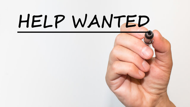the hand writes text HELP WANTED with a marker on a white background. business concept