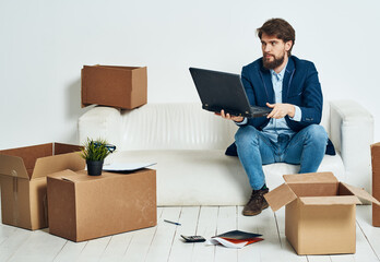Man sitting on sofa with laptop office boxes with things work