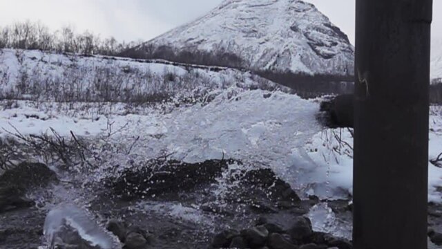 Water gushes from an artesian well enclosed in a pipe (bored tube well) in the middle of a mountainous area. Winter and freezing of ice and snow on the bush .Super slow motion 1000 fps.
