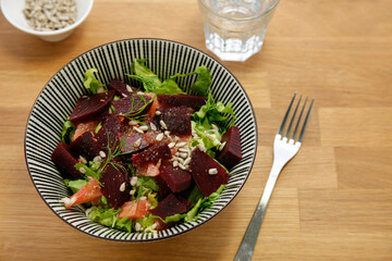 Wood table with fresh beetroot salad, suflower seeds and grapefruits, fork and water on the side, no person