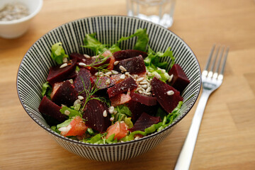 Fresh beetroot salad with suflower seeds and grapefruits, fork and water on the wooden table, no person
