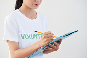 Cropped image of young woman in volunteer shirt filling documents when organizing event for community