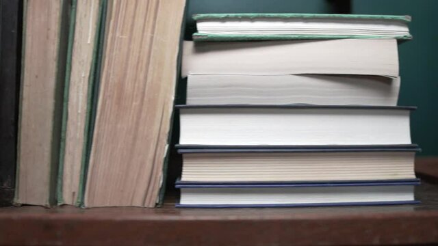 Stacks and piles of books on a wooden shelf supported by an elephant book end. Slow motion dolly pan shot.
