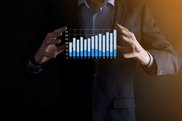 Business man holding holographic graphs and stock market statistics gain profits. Concept of growth planning and business strategy. Display of good economy form digital screen.
