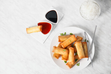 Plate with tasty fried spring rolls and sauce on light background