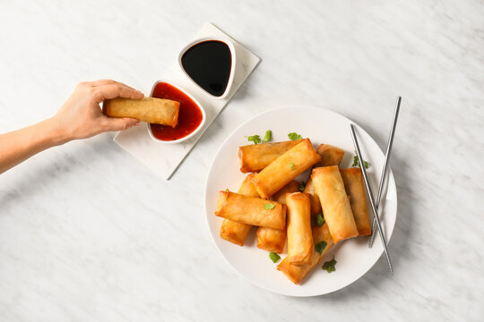 Woman eating tasty fried spring rolls with sauce on light background