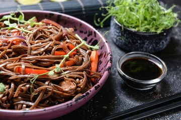 Plate with tasty soba noodles and meat on dark background
