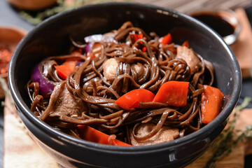 Plate with tasty soba noodles and meat on dark background