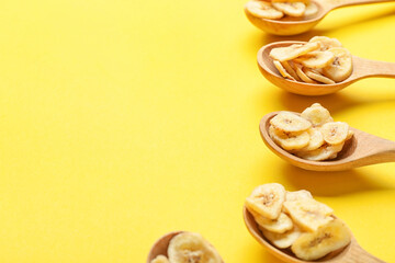 Wooden spoons with crispy banana chips on color background