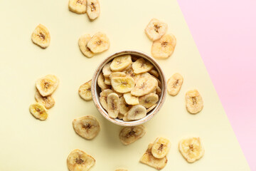 Bowl with crispy banana chips on color background