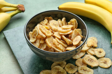 Fresh bananas and crispy chips on color background