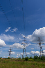 Pylons of high-voltage power transmission lines against a blue sky with white clouds