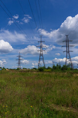 Pylons of high-voltage power transmission lines on a summer field with blue sky and clouds