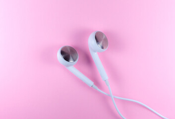 White Earphones lying on the pink background. Modern music concept. Audio technology. Close up photo.