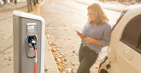 Close up of charging station on a background of a woman with a smartphone near an electric car