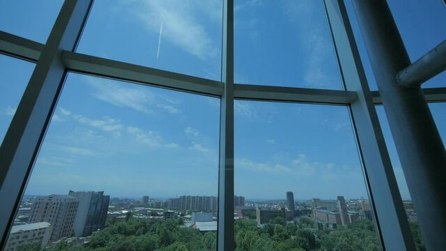 View of the city from a skyscraper glass elevator descending inside a business center with a glass roof. Elevator inside modern corporate office building, city center scenery - Slow Motion