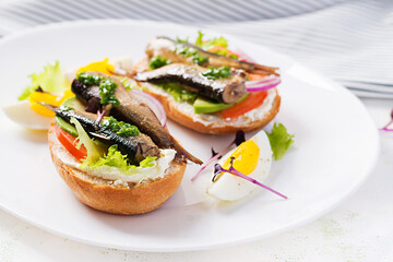 Sandwich - smorrebrod with sprats, avocado, tomatoes, eggs and cream cheese on white plate. Danish cuisine.  Eco friendly concept.