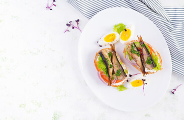 Sandwich - smorrebrod with sprats, avocado, tomatoes, eggs and cream cheese on white plate. Danish cuisine. Top view, overhead. Eco friendly concept.