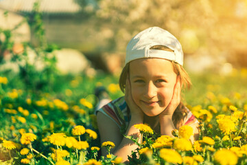 Closeup portrait of little cute girl lying with dandelions on the grass. Happy smiling girl lies on the grass among yellow flowering dandelions in the park. toned