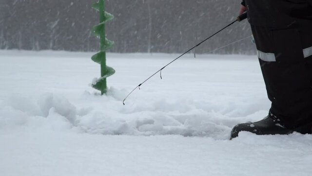 Winter fishing on ice. Man jiggling bait in an ice hole. Relaxing in the wild