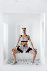 A young woman goes in for sports in a bright, minimalistic interior. Girl in the lotus position in the white architectural club