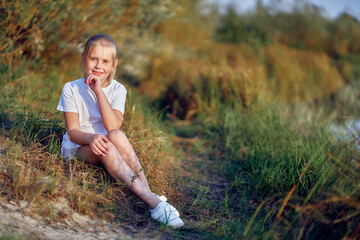 A 10-year-old girl sits on nature  by the path on a warm summer day.