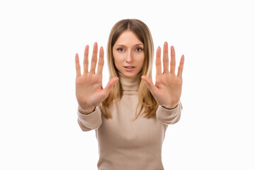 Serious blond girl keeps palms of both hands forward at camera, makes forbid sign, extends arms in...