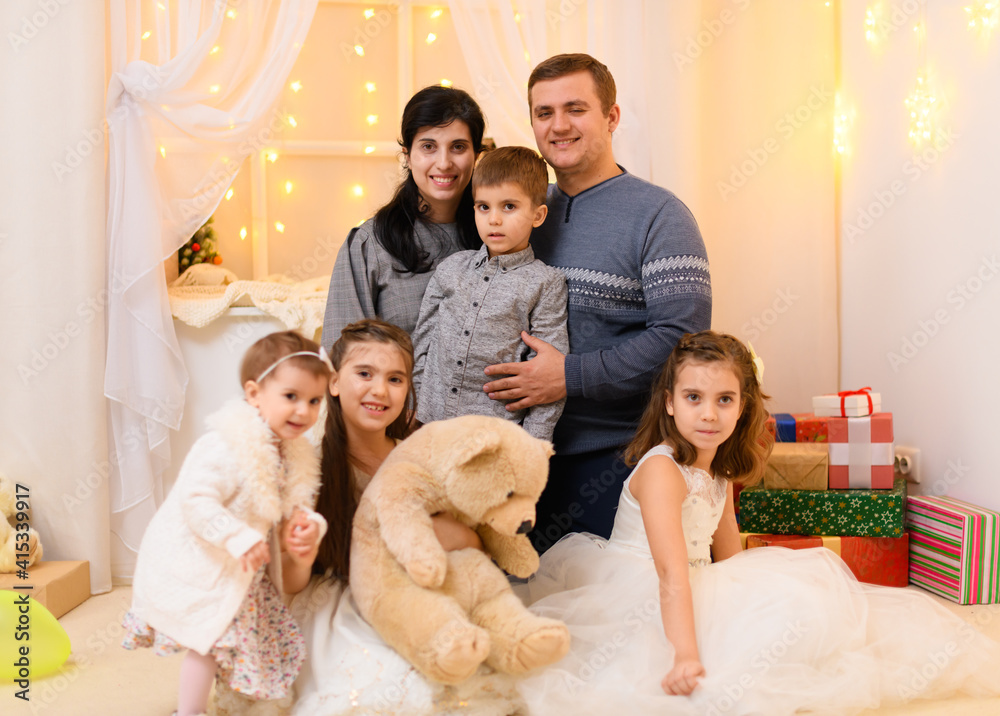 Wall mural family portrait - parents and children in home interior decorated with holiday lights and gifts