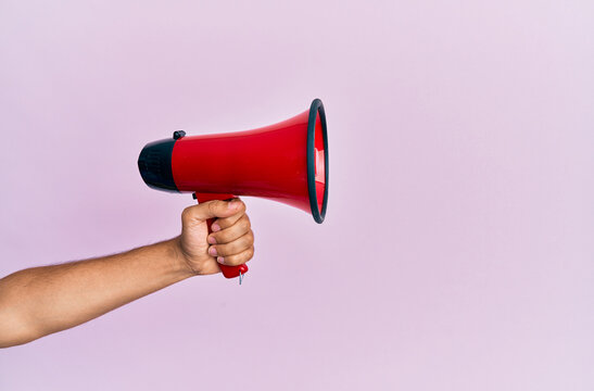 Hand of hispanic man holding megaphone over isolated pink background.