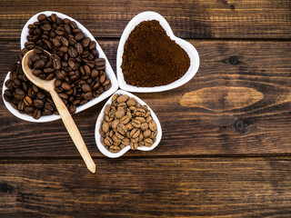 Coffee beans and ground on a wooden background in a white plate in the shape of a heart. Background and texture.