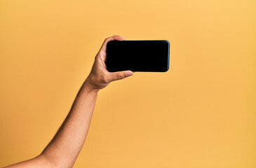 Fototapeta na wymiar Hand of young hispanic man showing smartphone over isolated yellow background.