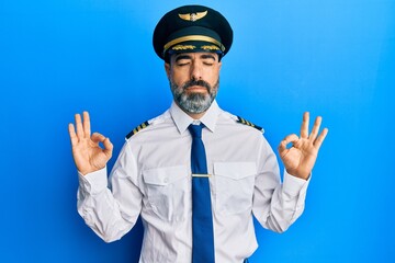 Middle age man with beard and grey hair wearing airplane pilot uniform relax and smiling with eyes closed doing meditation gesture with fingers. yoga concept.