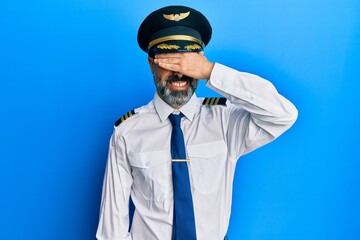 Middle age man with beard and grey hair wearing airplane pilot uniform smiling and laughing with...