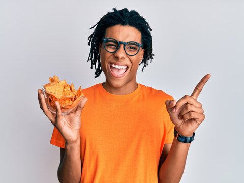 Young african american man holding nachos potato chips smiling happy pointing with hand and finger to the side