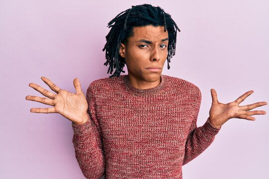 Young african american man wearing casual winter sweater clueless and confused with open arms, no idea and doubtful face.