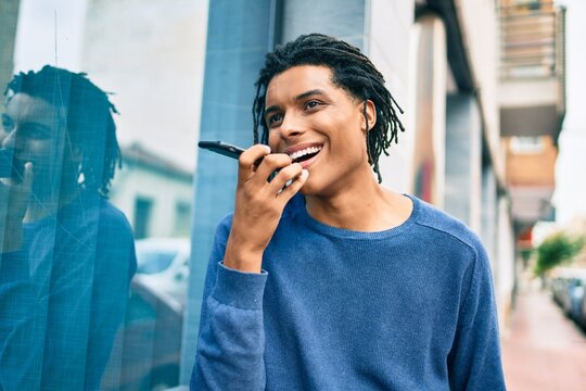Young african american man sending audio message using smartphone at street of city.