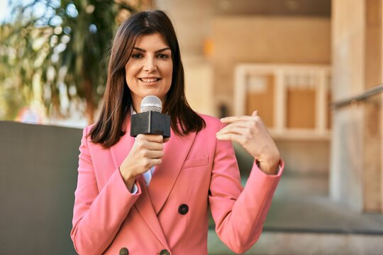 Middle age reporter woman holding microphone doing television speech outdoors
