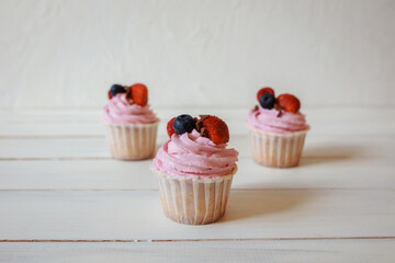 Sweet delicious cupcakes with whipped pink cream and fresh berries on the top.